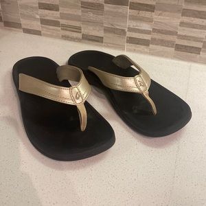 Olukai black and gold flip flops